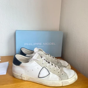 Philippe model  - Snygga vita sneakers från Philippe Model med mörk blåa detaljer och snörning. Skorna har en klassisk design med en smutsig look på sulan för en trendig stil. Perfekta för en avslappnad och stilren look. Nypris är runt 3500 kr! Skorna är i bra skick men det finns synligt slitage(speciellt sulan).Tyvärr inget kvitto. Hör gärna av er vid funderingar! /// Isak 