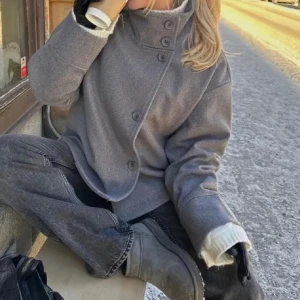 Grå kappa med knappar - Snygg grå kappa i ull med hög krage och stora knappar framtill. Jackan har en rak och lite loose passform, perfekt nu inför hösten. Enkel och stilren design som passar till det mesta. Långärmad och i mjukt material.