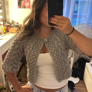 stickad bolero - Supermysig grå stickad kofta med grovt flätmönster och trekvartsärm. Koftan är croppad och stängs med en stor knapp vid halsen. Superfin att ha med ett linne som på bilden❣️❣️