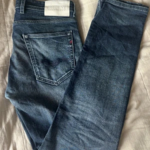 Replay Grover blå jeans herr - Snygga Replay Grover jeans i klassisk blå tvätt med lätt slitning. Modellen har raka ben, fem fickor och detaljer i silverfärgad metall. Tydlig Replay-logga på bakfickan och vit patch bak i midjan. Perfekta för dig som gillar en tidlös jeanslook.