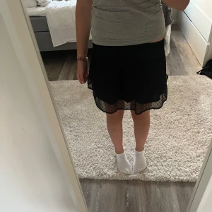 Svart volangkjol - Supersöt svart kortkjol med volanger. Kjolen har en smockad midja som sitter bekvämt och ger en snygg passform. I storlek 164 från H&M.