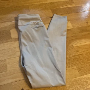 Beige leggings från 157 i storlek S - Snygga beige leggings från 157 med diskret logga vid höften. De är stretchiga och sitter tight, perfekta för träning eller chill. Tillverkade i ett mjukt och följsamt syntetmaterial som andas bra.