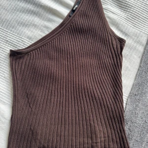 Ribbad one shoulder topp i brunt & beige - Två ribbade one shoulder-toppar från Bik Bok, en i mörkbrun och en i beige. Båda är ärmlösa och har en tight passform med bred ribbstickning. Materialet är strechigt. Pris kan diskuteras. 