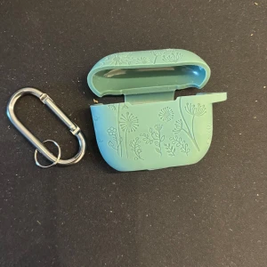 Grön AirPods-fodral från Lerobo - Säljer då det Står att den ska passa AirPods 3rd generation men funkar inte på dem, tror att de är för AirPods Pro. (Aldrig använt mer än provat).                                                  Snyggt grönt AirPods-fodral från Lerobo med ingraverade blommor och medföljande karbinhake. Tillverkat i mjuk silikon som skyddar dina hörlurar med top och botten som sitter ihop.