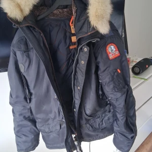 Parajumpers vinterjacka med päls - Mörkblå vinterjacka från Parajumpers med stor huva och fluffig pälsdetalj. Jackan har flera fickor, patch på ärmen och dragkedja framtill. Perfekt för kalla dagar och riktigt snygg streetstil.