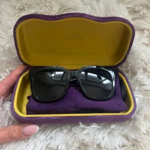 Svarta solglasögon från Gucci - Snygga svarta solglasögon från Gucci med fyrkantig form och klassisk guldig GG-logga på sidorna. Kommer med originalfodral i lila och gult samt en matchande lila putsduk. I jätte fint skick 