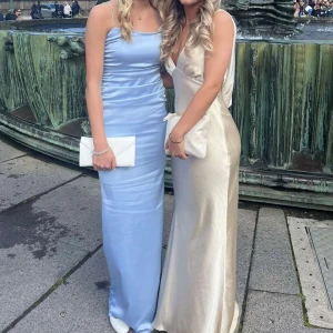 Champagnefärgad långklänning i satin - Säljer en elegant champagnefärgad långklänning i glansigt satinmaterial. Klänningen har djup v-ringning, smala axelband och en figurnära passform som faller snyggt längs kroppen. Perfekt för bal eller andra festligheter! Snygg och stilren look. (Jag är 164 och bär klackar på bilderna)🩷 sista bilden är lånad!!