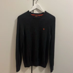 Mörkgrå merinoullströja Morris XS - Snygg mörkgrå stickad tröja från Morris i 100% merinoull. Klassisk modell med rund hals och lång ärm, prydd med Morris ikoniska orange brodyr på bröstet. Perfekt för dig som gillar stilrena och bekväma plagg. Hör av er vid minsta fundering🍾🍾🍾