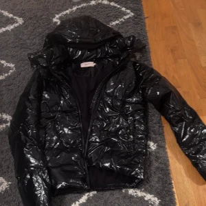 Svart glansig pufferjacka från Nelly - Säljer en svart glansig pufferjacka från Nelly i storlek XXS. Jackan har huva, dragkedja framtill och en riktigt cool, lite oversized look. Perfekt för dig som vill sticka ut med en trendig och varm jacka under kalla dagar.