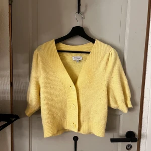 Gul kofta från & Other Stories - Superfin ljusgul kofta från & Other Stories med trekvartsärmar och stora knappar framtill. Koftan är stickad i mjukt material och har en bred ribbad kant vid halsen och nederkanten. Perfekt för att liva upp din outfit med en poppig färg.