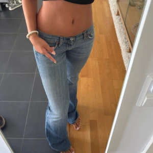 Blå bootcut jeans - Säljer ett par klassiska blå bootcut jeans med låg midja. Jeansen har fickor, snygga slitningar och subtila detaljer på bakfickorna. Perfekt passform och sköna att bära till vardags. Från 7forallmankind