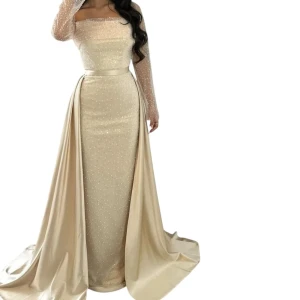 Champagnefärgad långklänning med pärlor - Säljer en elegant champagnefärgad långklänning med pärlprydd mesh upptill och långa ärmar. Klänningen har en figurnära siluett, markerad midja och ett svepande släp. Materialet är glansigt och ger en lyxig känsla, perfekt för bal,  nyår eller förlovning. Storlek 38-40