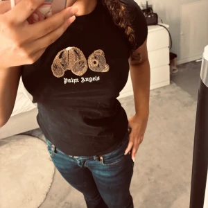 Svart Palm Angels t-shirt med nalle - Svart t-shirt från Palm Angels med ikoniskt nalletryck framtill och vit logga under. Modellen är klassisk med rund hals och korta ärmar. Materialet är mjuk bomull som sitter skönt mot kroppen. Perfekt för dig som gillar streetwear och vill sticka ut med en cool detalj.
