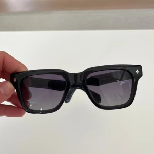 Svarta fyrkantiga solglasögon - Snygga svarta solglasögon med bred båge och fyrkantig form. Glasen är mörka och bågarna har små silvriga detaljer vid hörnen. Glasögonbox ingår.