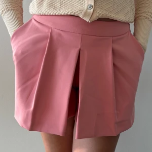 Korallrosa shortskjol från Zara Woman - Superfin korallrosa shorts/kjol från Zara Woman med  veck framtill. Tillverkad i ett mjukt och lätt material. Endast använd en gång 