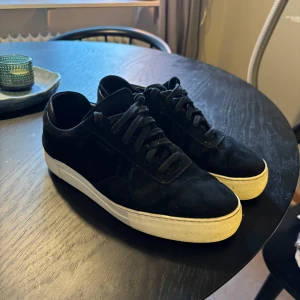 Axel Arigato - Snygga svarta sneakers från Axel Arigato med klassisk låg profil och vit platt sula. Skorna har mockaöverdel, rund tå och svart snörning. Perfekt för dig som gillar stilrena och minimalistiska sneakers med premiumkänsla.