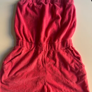 Rosa  ärmlös kort jumpsuit i frotté - Säljer en rosa , ärmlös kort jumpsuit i mjuk frotté. Klänningen har resår i midjan för en skön passform och praktiska fickor på sidorna. Perfekt för varma dagar och enkel att slänga på sig när du vill vara bekväm men ändå snygg.