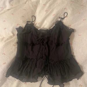 Svart volangig snörad topp från Zara - Supersöt svart topp från Zara med volangdetaljer och snörning framtill. Tunt, flowigt material med smala axelband och lätt rynkade sömmar.