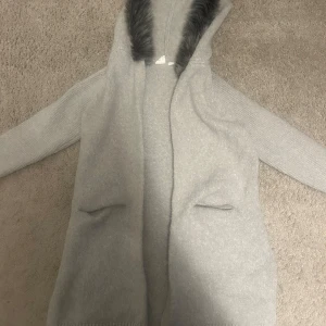 Ljusgrå cardigan  - Mysig ljusgrå cardigan jacka från GAP med huva och fuskpälsdetalj runt kanten. Jackan är stickad, har två fickor framtill och långa ärmar. Perfekt för lager-på-lager och chill dagar. Storlek m men är mindre i storleken så jag skulle beskriva den som xs 