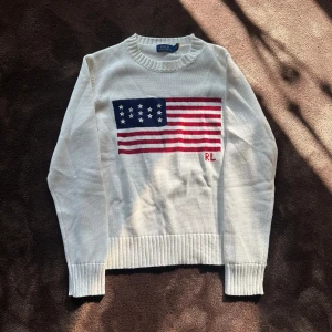 Vit stickad tröja Polo Ralph Lauren - Vit stickad tröja från Polo Ralph Lauren med amerikansk flagga i blått, rött och vitt på bröstet samt RL-broderi. Rund hals och ribbade muddar vid ärmslut och nederkant. Perfekt för dig som gillar klassisk och cool stil. OBS! Hjälper min syrra sälja sin tröja. Kvinno storlek!! M. VET EJ I HERR. KANSKE XS. Pris kan diskuteras. Dock använd ett par gånger men inga tecken på det. Fungerar lika bra om man har S. 