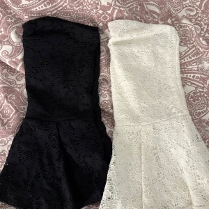 Svart och vit spetsklänning axelbandslös - Två tubtoppar  i svart och vit, båda med blommigt spetsmönster. Toppen har en figurnära passform upptill och lätt utsvängd kjol. Perfekt för dig som gillar romantisk stil och vill sticka ut med snygga detaljer. ST STÅR INTE, men skulle säga S-M 