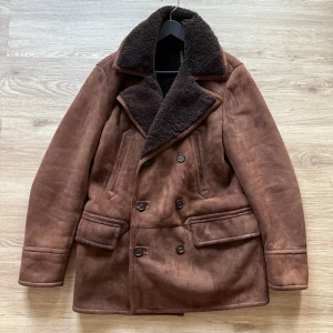 Ralph Lauren purple label jacka - Purple Label's elevated take on the timeless peacoat is crafted in Italy from soft shearling.  Long sleeves with clean-finished cuffs.  Two chest welt pockets. Two front waist flapped pockets.  Single vent.  Unlined.  Dry clean by a shearling specialist.  100% dyed sheep shearling. Made in Italy.  Shearling origin: Spain.  Model is 1.85 m and wears a size M.  Style Number: 634761  Note: small stains on the sleeves they should go away if you wash it