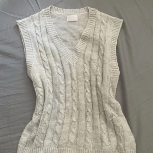 Stickad ljusbeige väst - Stickad väst i ljusbeige ton med klassiskt flätmönster framtill och ribbade kanter. V-ringad hals och mjukt material som känns chill och stilrent. Perfekt att slänga över en skjorta för en stilren look. Jag har svårt att tyda vilket märke det är. Ursprungs pris ca 400-600 kr. Aldrig använd.
