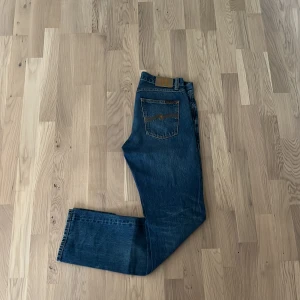Blå jeans från Nudie Jeans Co - Snygga blå jeans från Nudie Jeans Co med klassisk femficksdesign och orangea sömmar. Jeansen har rak passform och är tillverkade i slitstarkt bomullsjeans. Perfekta för dig som gillar en tidlös och avslappnad look.