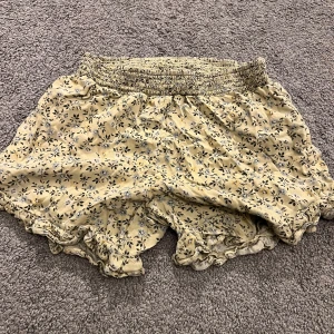 Gula blommiga shorts med volang - Söta gula shorts med blommigt mönster och volangkant. De har en bred, smockad midja som är superstretchig och bekväm. Perfekta för varma dagar och ger en chill och somrig vibe. Lätta och luftiga i materialet.