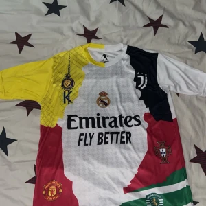 CR7 Ronaldo collage fotbollströja - Unik fotbollströja med collage av Ronaldo-klubbar: Real Madrid, Juventus, Manchester United, Sporting Lissabon och Portugal. Flera färger som vit, gul, svart, röd och grön. Kortärmad, tillverkad i glansigt polyestermaterial. Tryck med 'Emirates Fly Better', 'Ronaldo' och nummer 7.