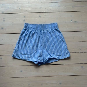 Blå randiga poplin shorts - Snygga randiga shorts tillverkade i mjuk bomull. De har elastisk midja för skön passform och en loose siluett. Perfekta för varma dagar och passar dig som gillar enkel och stilren design. I fint skick.