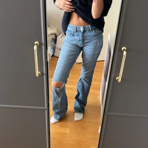 Blå bootcut jeans från Gina Tricot - Säljer ett par blå bootcut jeans från Gina Tricot, modell Perfect Jeans. De har en snygg sliten look med hål på ena knät och klassisk femficksdesign. Jeansen är i denim och har normal passform med medel midja.