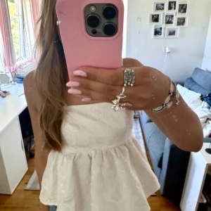 Vit blommig linnetopp med knyt - Supersöt vit linnetopp med blommigt mönster i strukturen. Toppen har smala axelband, volangig peplum-nederdel och snygg knytning i ryggen med öppen detalj. Perfekt för sommarens alla tillfällen och ger en fräsch och romantisk vibe.