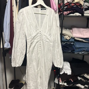 Virala Vita långklänningen ifrån Gina tricot - Supersnygg vit långklänning från Gina Tricot med broderade blommor, v-ringad front och puffiga långärmar. Klänningen har knappar framtill och en dragkedja i ryggen. Använd i få timmar, som ny!