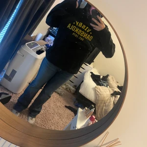 Svart hoodie Visby Dansskola - Svart hoodie med gul text 'Visby Dansskola Est. 1975' på bröstet. Klassisk modell med huva och snörning, samt långärmad. Perfekt för dig som gillar streetstyle och vill ha något bekvämt och snyggt.