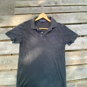 Svart pikét från U.S. Polo Assn - Svart piké från U.S. Polo Assn i bomull, med klassisk krage och två knappar framtill. Liten lila broderad logga på bröstet. Passar 170-180cm Hör av dig frågor!