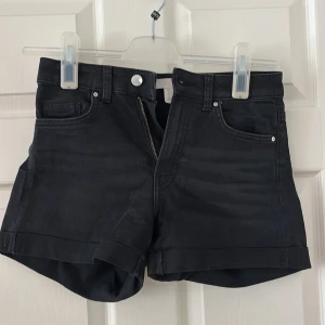 Svarta jeansshorts från H&M - Snygga svarta jeansshorts med hög midja och klassisk femficksdesign. De har uppvikta benslut och dragkedja framtill. Perfekta för dig som gillar en enkel och stilren look med lite edge. Passar till allt och är superenkla att matcha med dina favoritplagg.