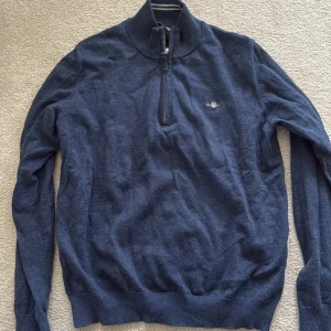 Marinblå half zip tröja från Gant - Snygg marinblå långärmad tröja från Gant med half zip och hög krage. Tröjan har broderad logga på bröstet och är tillverkad i mjukt stickat material. Perfekt för dig som gillar klassisk och stilren look.