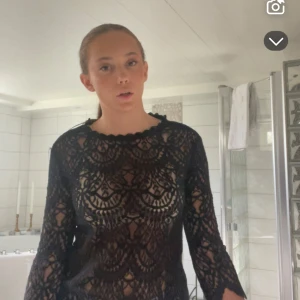 Svart spetsblus med 3/4-ärm - Säljer en svart blus i spets med snyggt mönster och 3/4-långa ärmar. Blusen har rundad hals och transparent design som ger en cool vibe. Perfekt att styla med jeans eller kjol för en trendig look. Spetsen har ett detaljerat och unikt mönster.