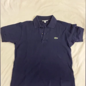 Marinblå Lacoste Classic Fit pike  - Snygg marinblå piké  från Lacoste i klassisk pikémodell med krage och knappar framtill. Ikonisk broderad krokodil på bröstet. Classic Fit och tillverkad i bomull som känns skön mot huden. Perfekt för dig som gillar stilrena och sportiga vibes. Franklin saint🫡