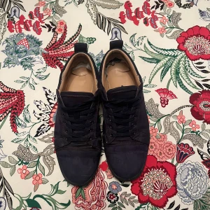 Christian Louboutin svarta mockasneakers - Snygga marin blå sneakers från Christian Louboutin i mocka med ikoniska röda sulor. Skorna har rund tå, marin blå snören och diskret broderad logga på hälen. Kommer med originalkartong, dustbag och äkthetskort. Perfekta för dig som vill sticka ut med lyxig streetstyle.