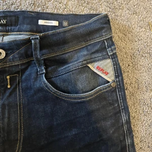 Replay Anbass jeans - Säljer ett par Replay Anbass jeans i mörkblå tvätt med snygga kontrastsömmar och klassisk femficksdesign. Jeansen har en slim passform och är tillverkade i stretchig bomullsdenim för extra komfort. Perfekta för dig som gillar stilrena och moderna jeans.