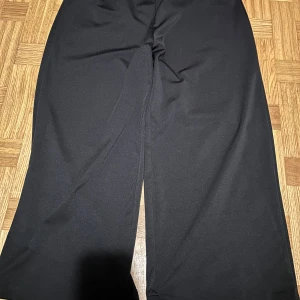 Svarta wide byxor i polyester XXL - Svarta byxor i storlek XXL med breda ben och elastisk midja. Tillverkade i 95% polyester och 5% spandex för en skön och stretchig känsla. Perfekta för dig som gillar en loose och avslappnad stil.