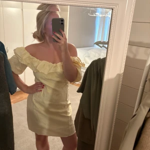 Gul kort offshoulder klänning med volang - Säljer en ljusgul kort klänning med offshoulder och bred volang runt halsen. Klänningen har en somrig vibe, med puffiga ärmar och figurnära passform. .