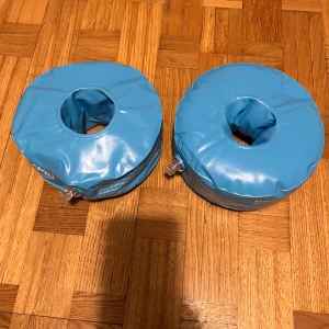 Blå badarmringar från Aquarapid - Säljer ett par blå badarmringar från Aquarapid, passar upp till 30 kg. De är runda och uppblåsbara med ventiler för enkel påfyllning. Perfekta för simträning eller lek i poolen. Snygg och enkel design med vit logga på sidan.