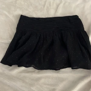 Svart prickig kjol från Gina Tricot - Supersöt svart kortkjol från Gina Tricot med små diskreta prickar och ett rynkat midjeband. Kjolen har en lätt volangig form och är gjord i ett tunt, flowy material som ger en skön känsla. Perfekt för dig som gillar en enkel men ändå stylish look.