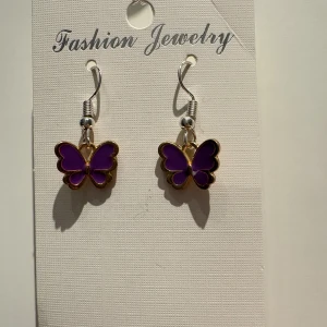 Lila fjärilsörhängen med guldkant - Superfina örhängen med lila fjärilar och guldfärgade kanter. Hängande modell med silvriga krokar som ger en snygg kontrast. Perfekt för dig som vill ha något unikt och färgglatt i öronen.