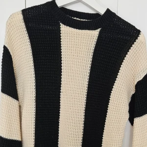 Svart och beige stickad tröja med breda ränder - Säljer en stickad tröja med breda svarta och beige ränder. Tröjan har lång ärm och en klassisk rund halsringning. Perfekt för dig som gillar en stilren och trendig look.