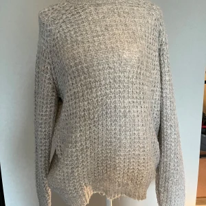 Grå stickad tröja  - Mysig grå stickad polotröja med grov struktur och lång ärm. 