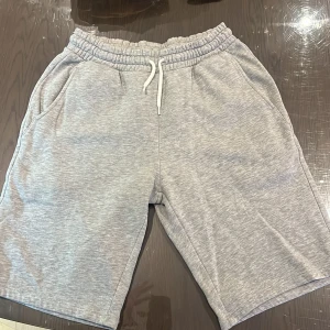 Grå mjukisshorts från Lindex - Gråa mjukisshorts från Lindex med resår och snörning i midjan. Shortsen har två sidofickor och är tillverkade i ett mjukt material som passar perfekt för avslappnade dagar.